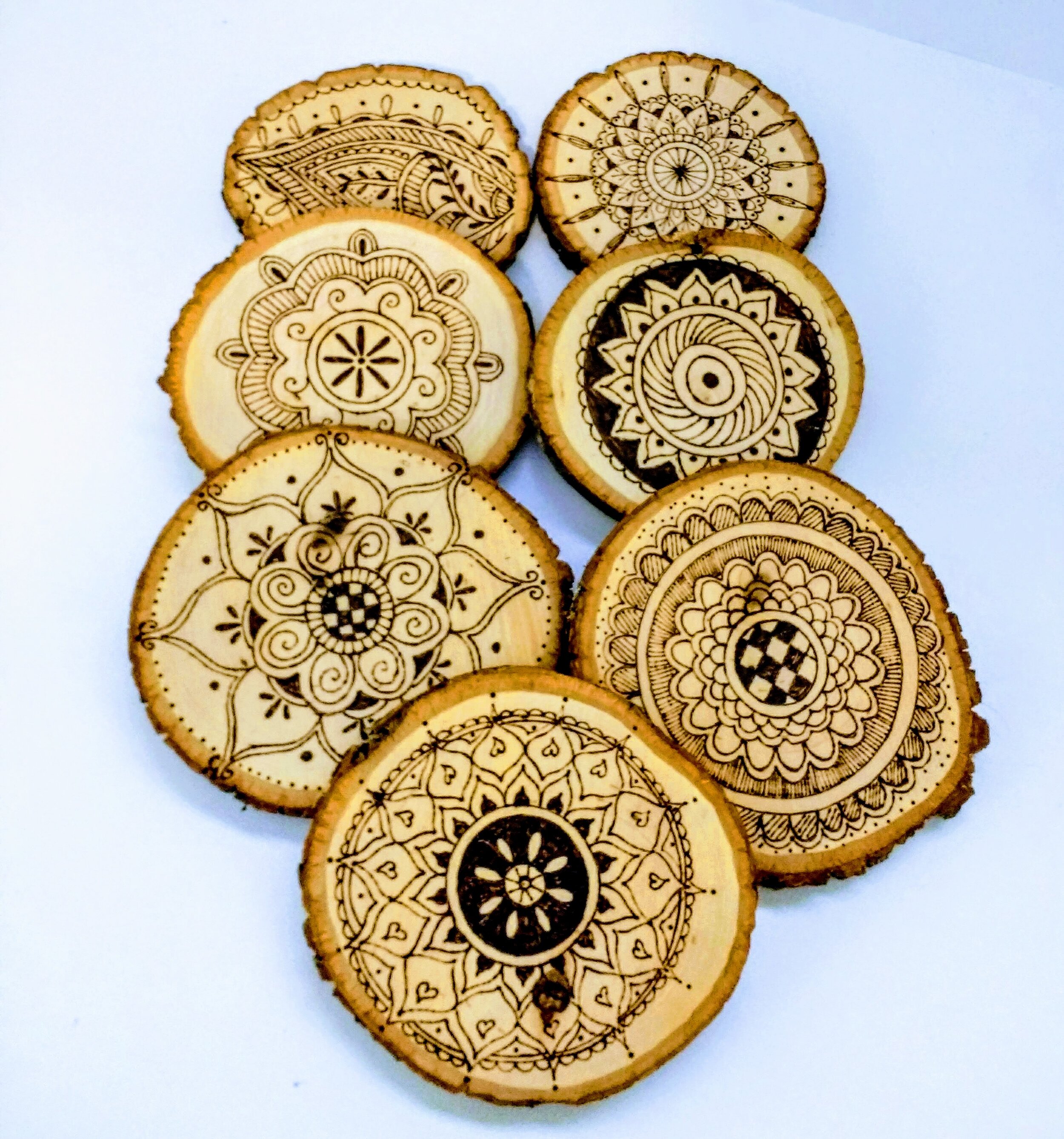 Seven pieces of circular wood feature a variety of mandala art that has been wood burned