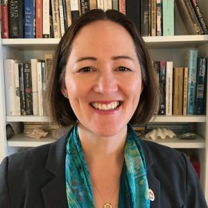 Headshot of Professor Yoshiko Herrera. She is smiling and wearing a charcoal blazer and teal scarf with books on shelves in the background.