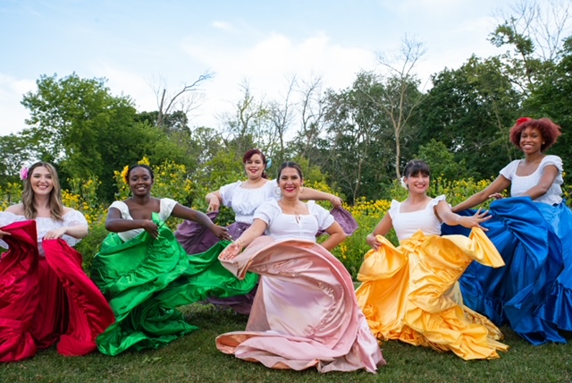 6 diverse women wearing dresses with white bodices and different colored flowing skirts (red, green, pink, yellow, blue) swirling their skirts and smiling outdoors